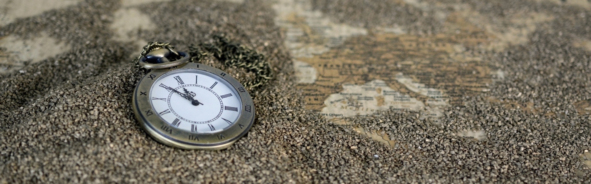 Taschenuhr im Sand auf einer Landkarte – Symbol für den richtigen Zeitpunkt der Unternehmensplanung